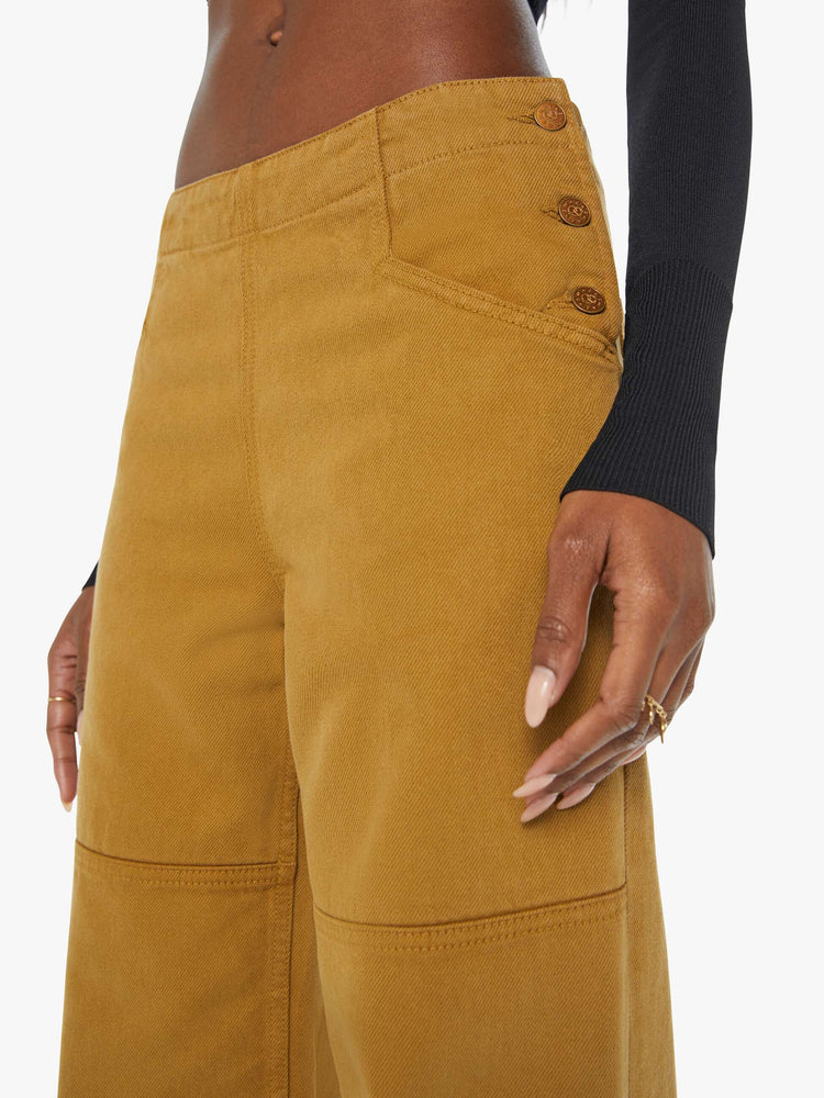 Detailed view of a woman in golden khaki wide-leg pants designed with a high rise, buttons at the hips, workwear-inspired patches at the knees, utility pockets, and a hammer loop.