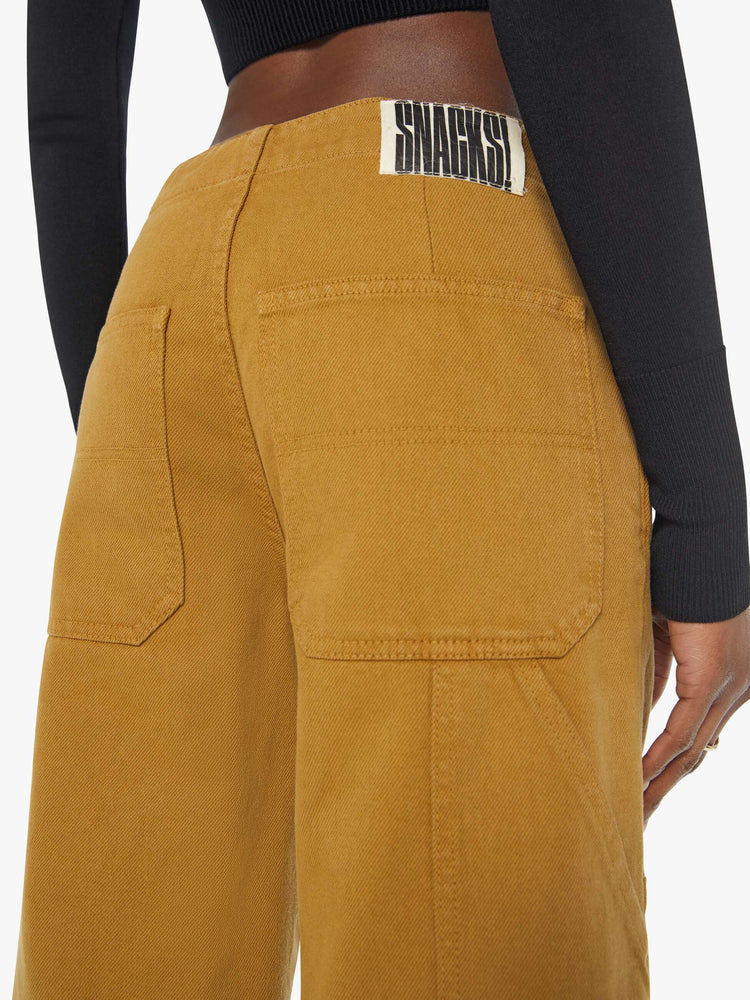 Back view of a woman in golden khaki wide-leg pants designed with a high rise, buttons at the hips, workwear-inspired patches at the knees, utility pockets, and a hammer loop.