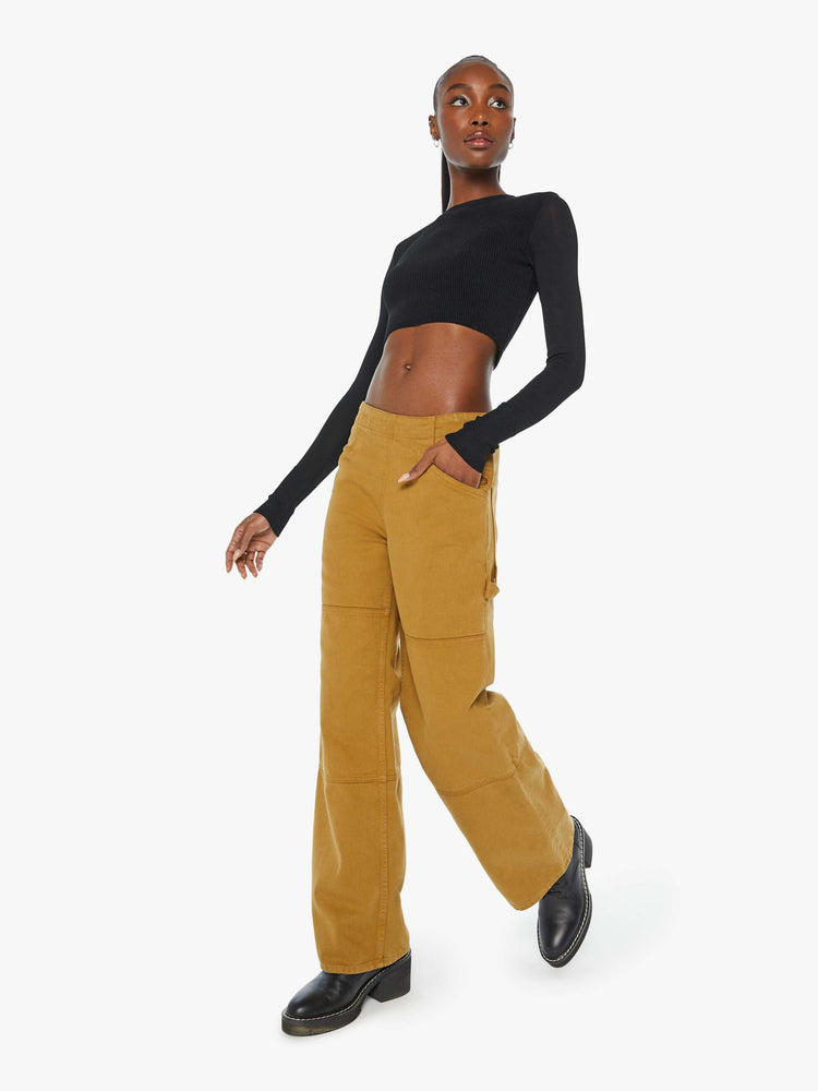 Angled front view of a woman in golden khaki wide-leg pants designed with a high rise, buttons at the hips, workwear-inspired patches at the knees, utility pockets, and a hammer loop.