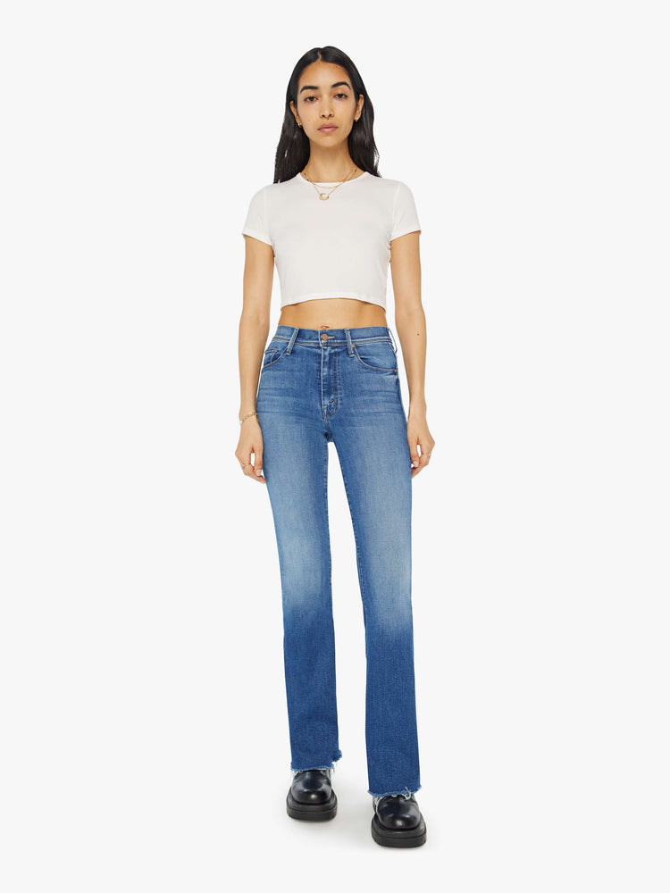 Full front view of a woman in mid-blue md-rise jeans with a flared leg, long 32-inch inseam and a frayed hem.