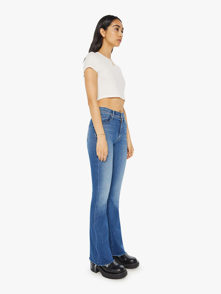 Angled front view of a woman in mid-blue md-rise jeans with a flared leg, long 32-inch inseam and a frayed hem.