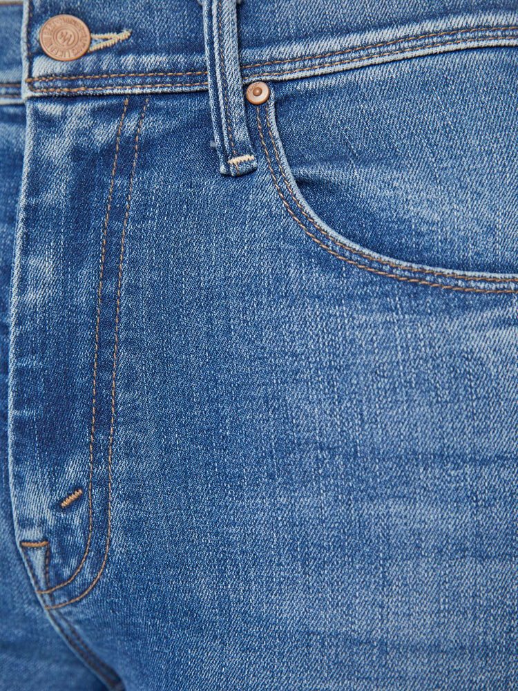 Detailed view of a woman in mid-blue md-rise jeans with a flared leg, long 32-inch inseam and a frayed hem.