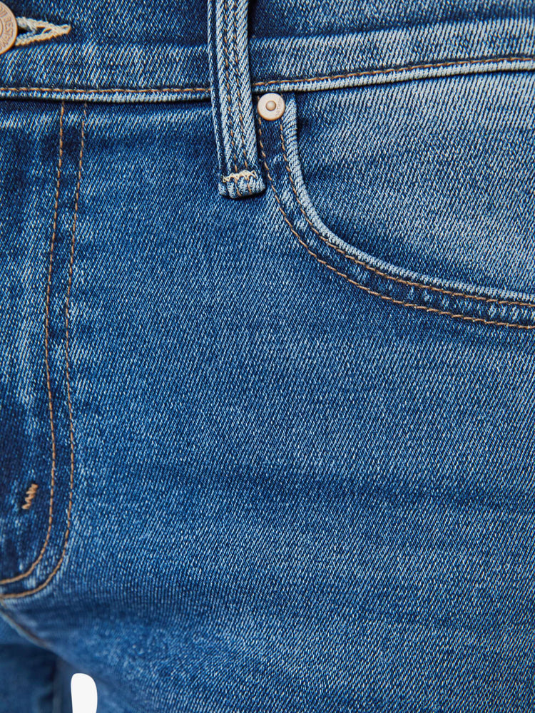 Swatch view of a woman in med blue mid-rise jeans with a wide straight leg, zip fly, an ankle-length inseam and a frayed hem.