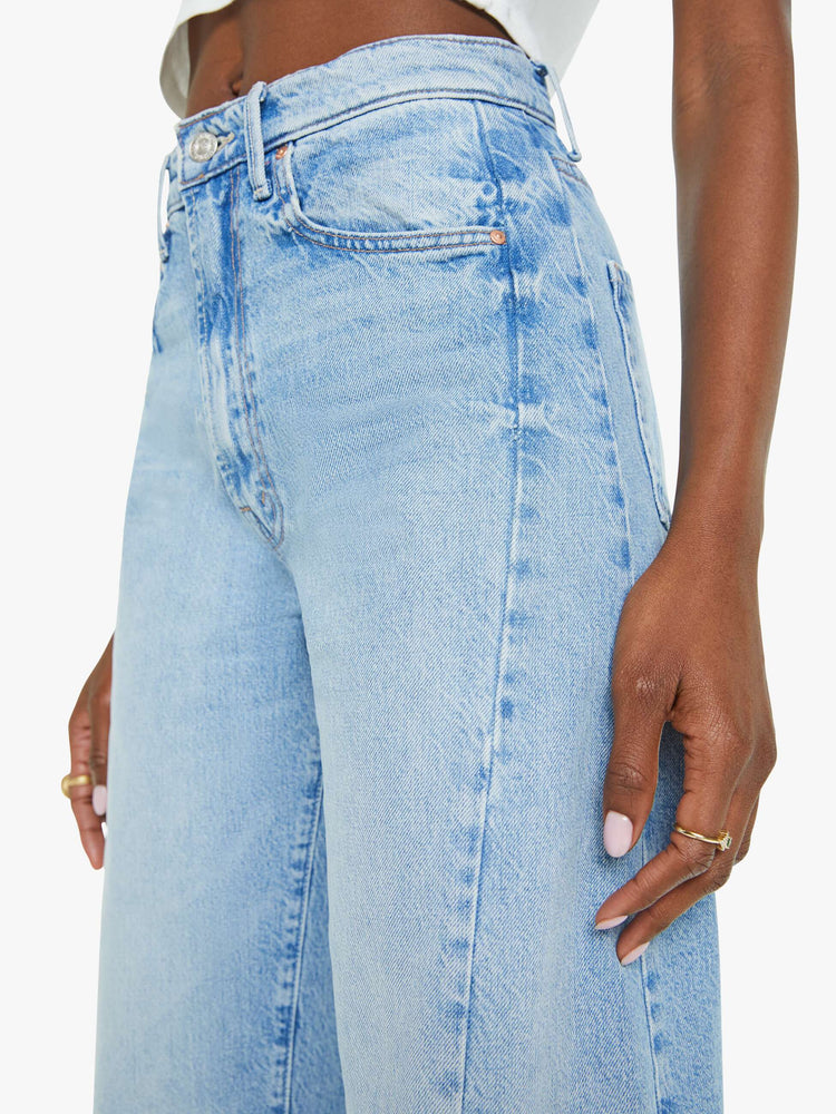 Side close up view of a woman super high-waisted jean with a wide, curved leg, an ankle-length inseam and a clean hem in a light blue wash.