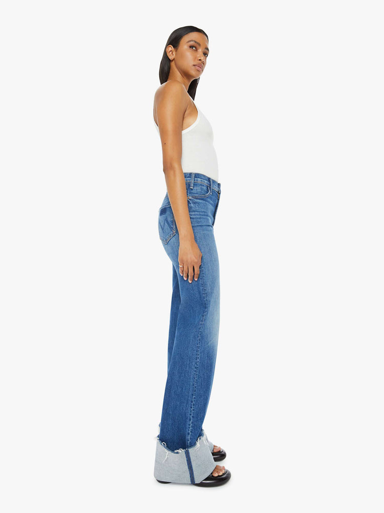 Side view of a woman wide leg jeans with a high rise, long 34-inch inseam and an oversized cuffed hem that's frayed in medium blue wash. 