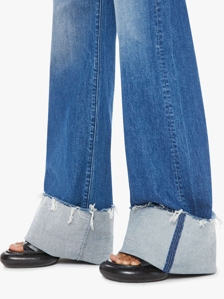 Hem view of a woman wide leg jeans with a high rise, long 34-inch inseam and an oversized cuffed hem that's frayed in medium blue wash. 