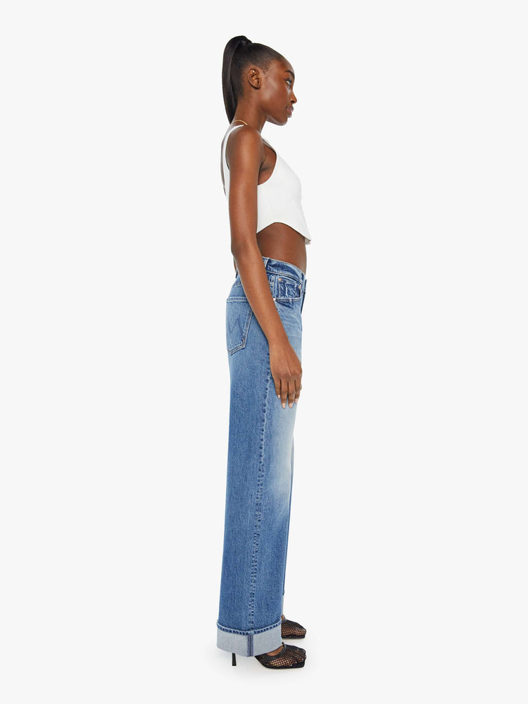 Side view of woman in a mid blue wash jean designed to sit lower on the hips with a loose straight leg and a 31-inch inseam with a clean cuffed hem.