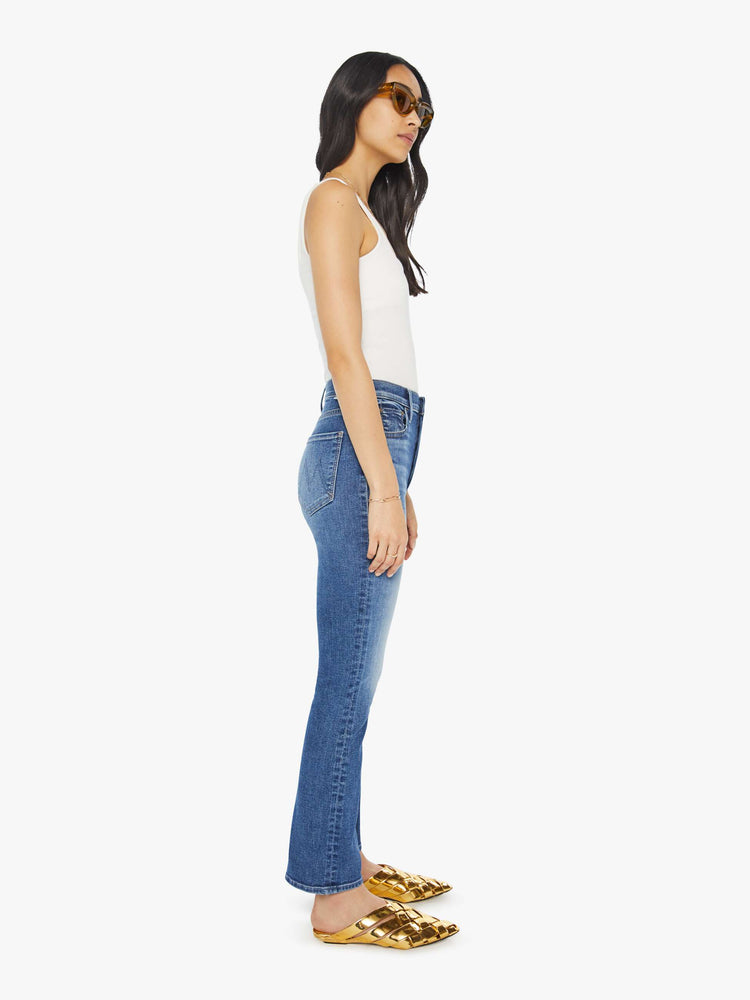 Side view of a woman in mid blue wash high-rise flare with a button fly and 28.25-inch inseam with a clean hem.