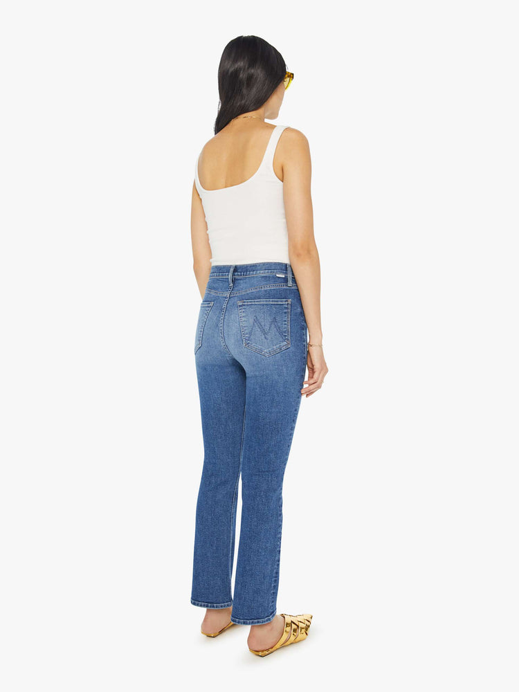 Back view of a woman in mid blue wash high-rise flare with a button fly and 28.25-inch inseam with a clean hem.