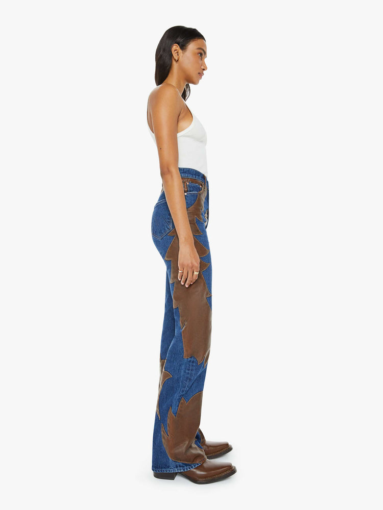 Side view of a woman super high-waisted bootcut jeans with a 34-inch inseam and clean hem in a dark blue wash with a faux leather applique.