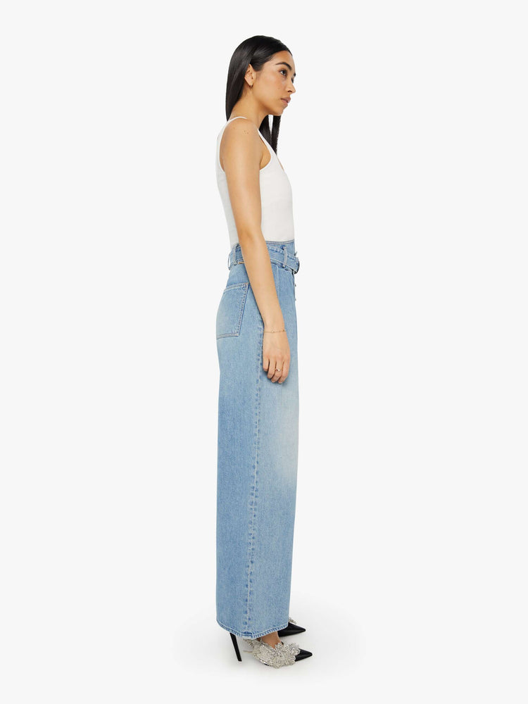 Side view of a light blue super high-waisted wide-leg jean features a belted waistband with pleats and angled details, an exposed button fly and a long 31-inch inseam with a clean hem.