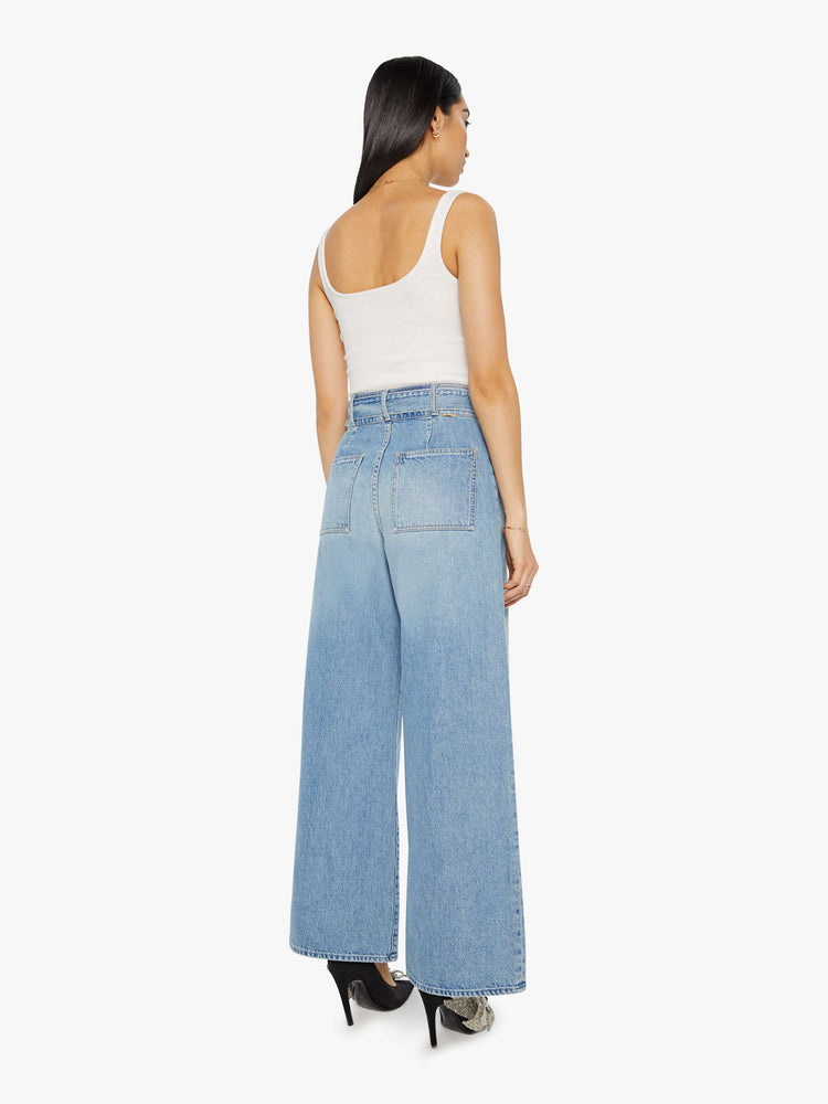 Back view of a light blue super high-waisted wide-leg jean features a belted waistband with pleats and angled details, an exposed button fly and a long 31-inch inseam with a clean hem.