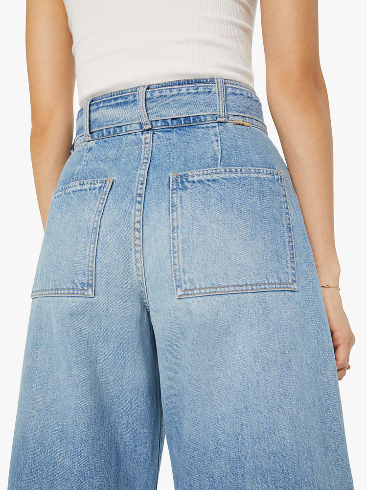 Close up back view of a light blue super high-waisted wide-leg jean features a belted waistband with pleats and angled details, an exposed button fly and a long 31-inch inseam with a clean hem.