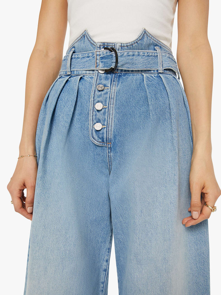 Front details view of a light blue super high-waisted wide-leg jean features a belted waistband with pleats and angled details, an exposed button fly and a long 31-inch inseam with a clean hem.