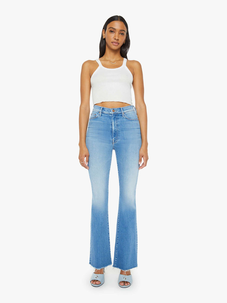 Front view of a woman in medium blue flare  jean has a high rise with a 31-inch length inseam and a frayed hem. 