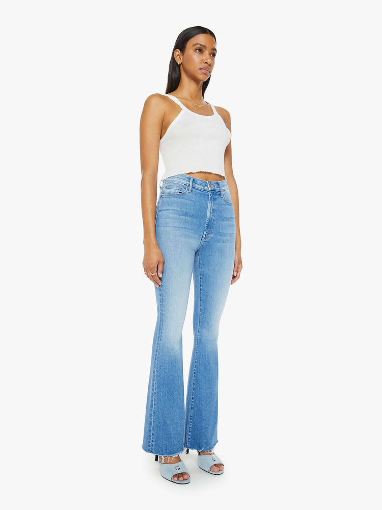 Side angle view of a woman in medium blue flare  jean has a high rise with a 31-inch length inseam and a frayed hem. 