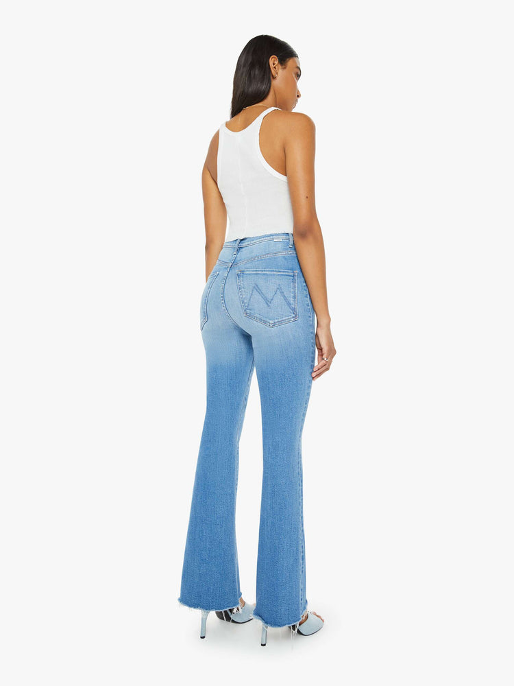 Back view of a woman in medium blue flare  jean has a high rise with a 31-inch length inseam and a frayed hem. 