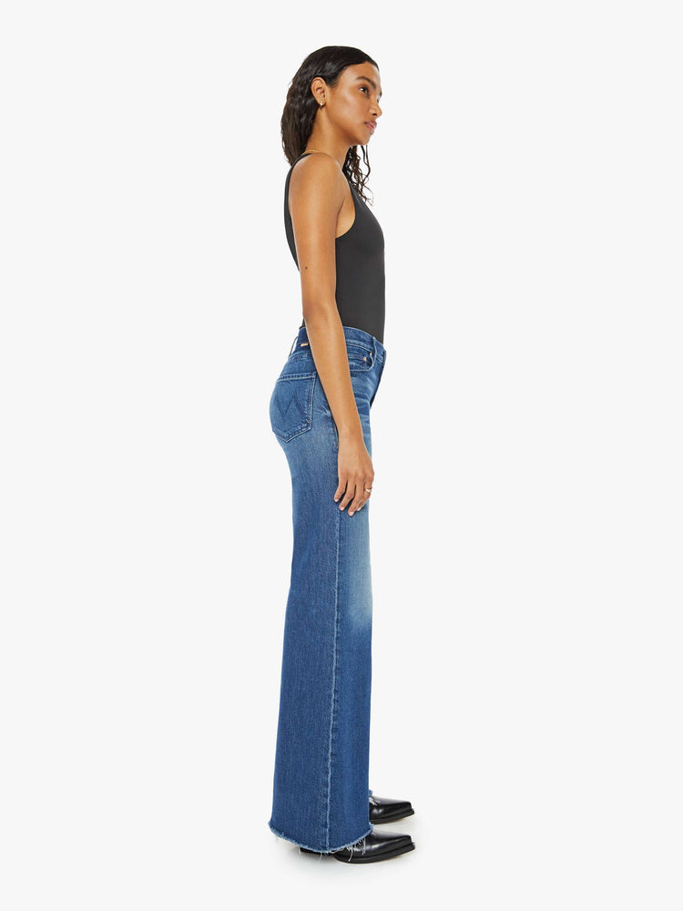 Side view of a med blue wash super wide-leg jeans with a high rise, a slouchy fit, flared leg and a long 32-inch inseam with a frayed hem.