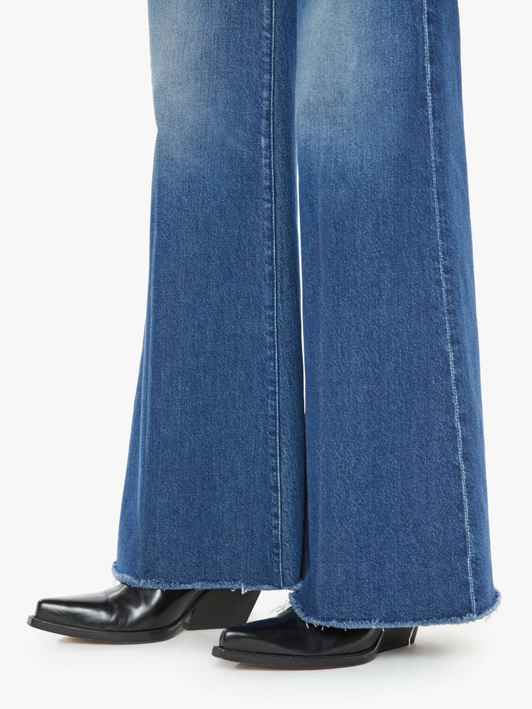 Hem close up view of a med blue wash super wide-leg jeans with a high rise, a slouchy fit, flared leg and a long 32-inch inseam with a frayed hem.