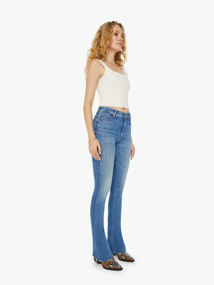 Side angle  view of a woman in mid blue mid-rise flare with a 34-inch inseam and a frayed hem.