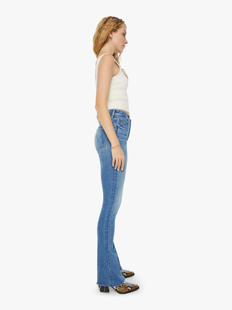 Side view of a woman in mid blue mid-rise flare with a 34-inch inseam and a frayed hem.