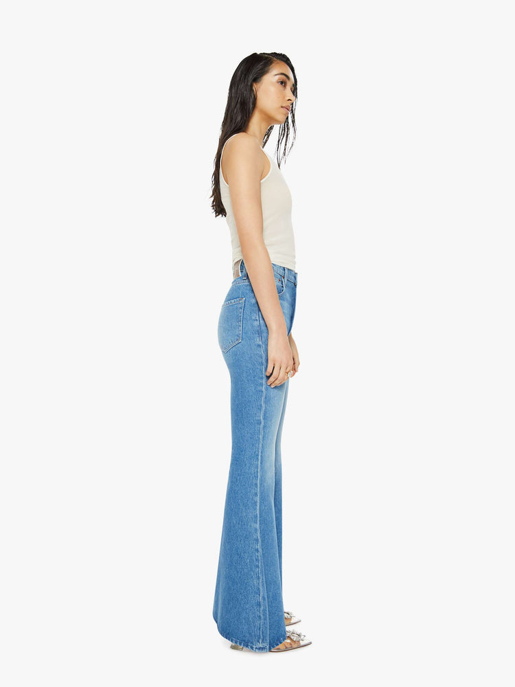 Side view of a woman in high-waisted light blue jeans have an extreme flare and a long 34-inch inseam with a clean hem. 