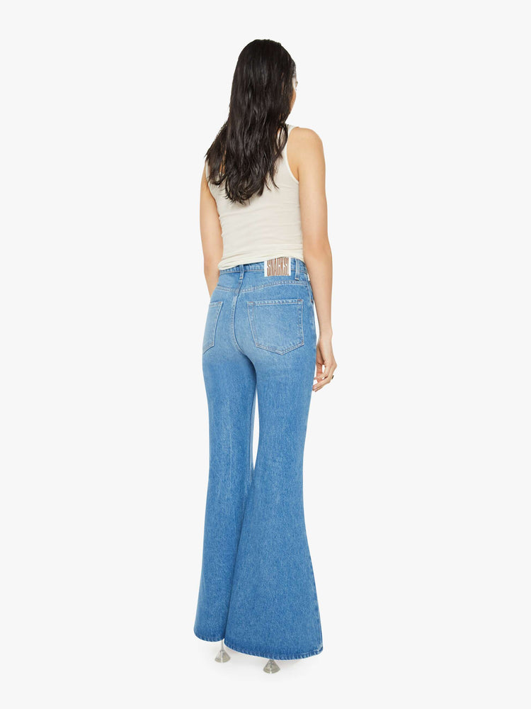 Back view of a woman in high-waisted light blue jeans have an extreme flare and a long 34-inch inseam with a clean hem. 