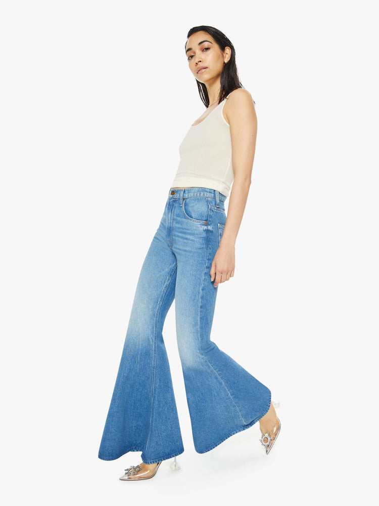 Walking view of a woman in high-waisted light blue jeans have an extreme flare and a long 34-inch inseam with a clean hem. 