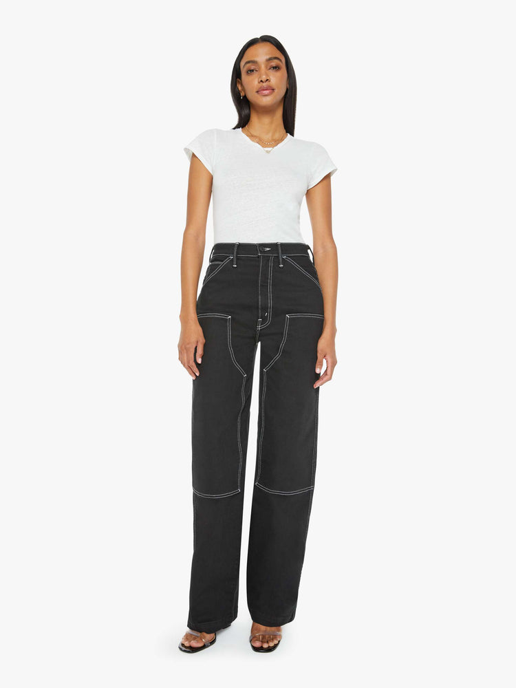 Front view of a woman super high-waisted pants with a wide leg, oversized patches at the knees, a long 32-inch inseam and a clean hem in black with white stitching.