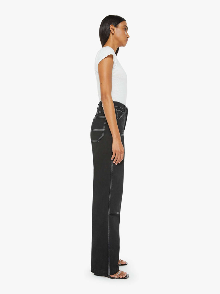 Side view of a woman super high-waisted pants with a wide leg, oversized patches at the knees, a long 32-inch inseam and a clean hem in black with white stitching.