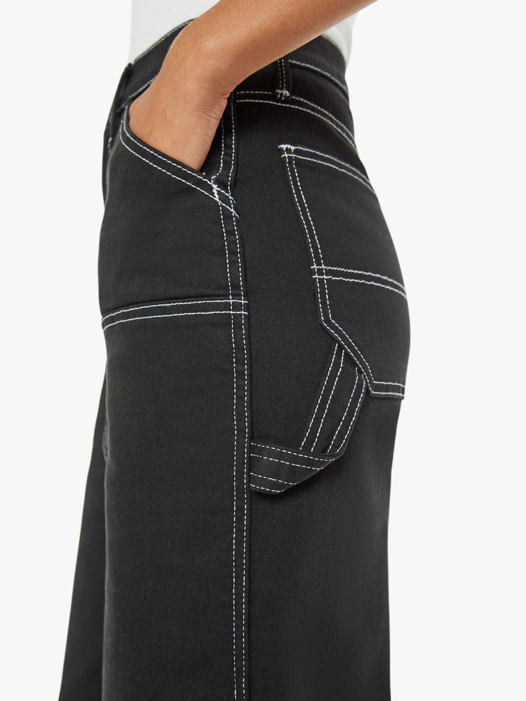 Close up view of a woman super high-waisted pants with a wide leg, oversized patches at the knees, a long 32-inch inseam and a clean hem in black with white stitching.