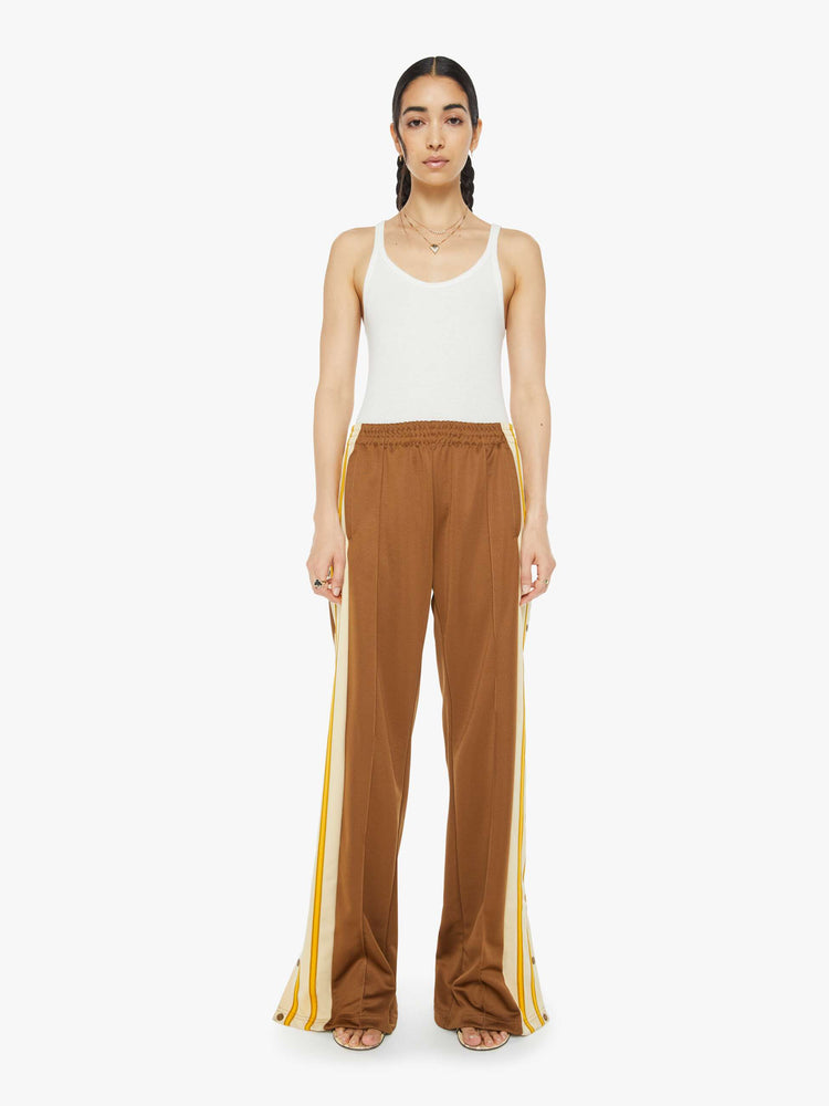 Front view of a woman in track pant features a high rise, wide leg, elastic waistband, slit pockets that zip, a long 34-inch inseam and a seamed detail down the front in light brown.