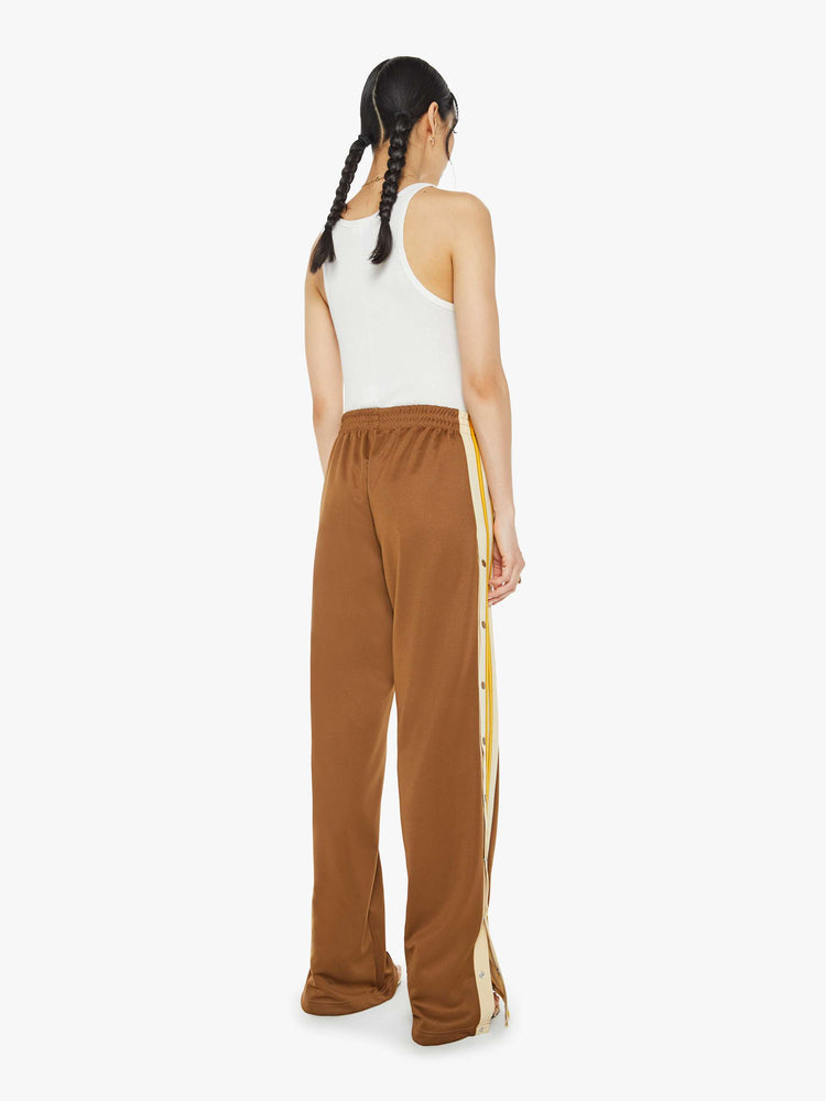 Back view of a woman in track pant features a high rise, wide leg, elastic waistband, slit pockets that zip, a long 34-inch inseam and a seamed detail down the front in light brown.