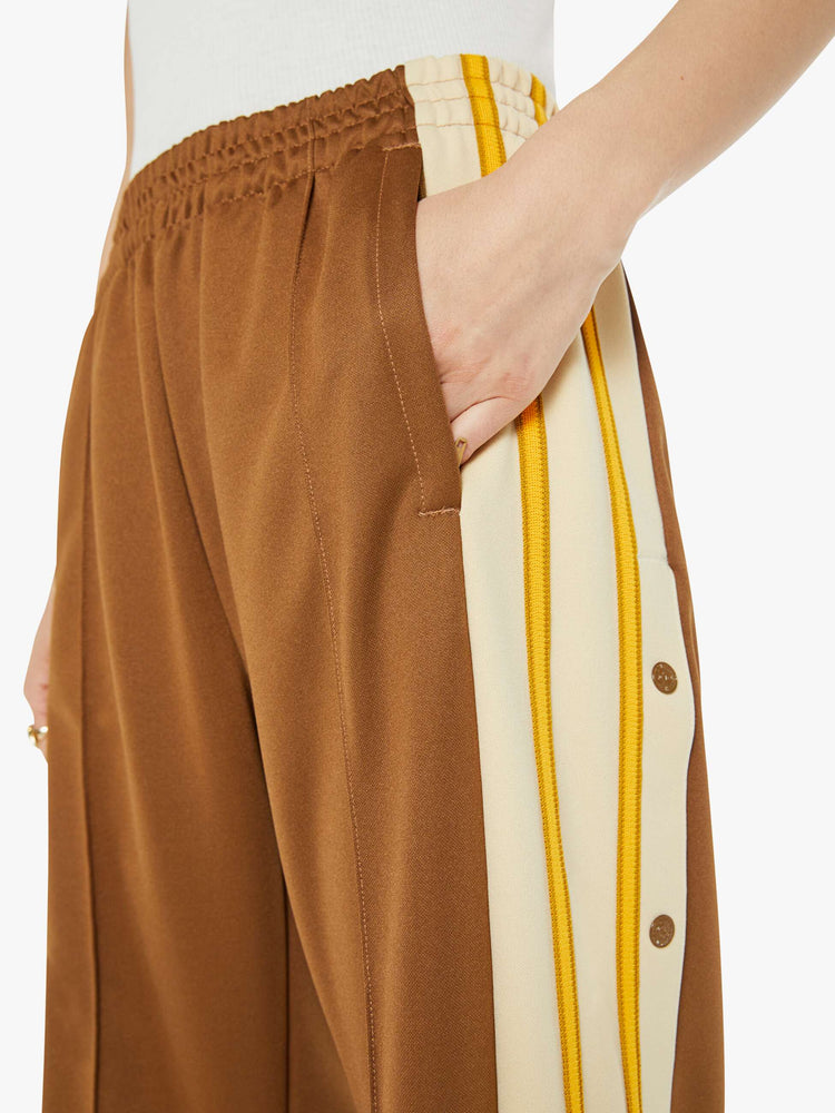 Close up view of a woman in track pant features a high rise, wide leg, elastic waistband, slit pockets that zip, a long 34-inch inseam and a seamed detail down the front in light brown.