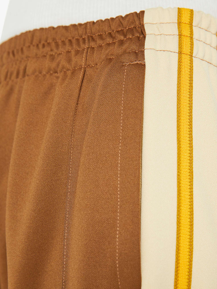 Swatch view of a woman in track pant features a high rise, wide leg, elastic waistband, slit pockets that zip, a long 34-inch inseam and a seamed detail down the front in light brown.