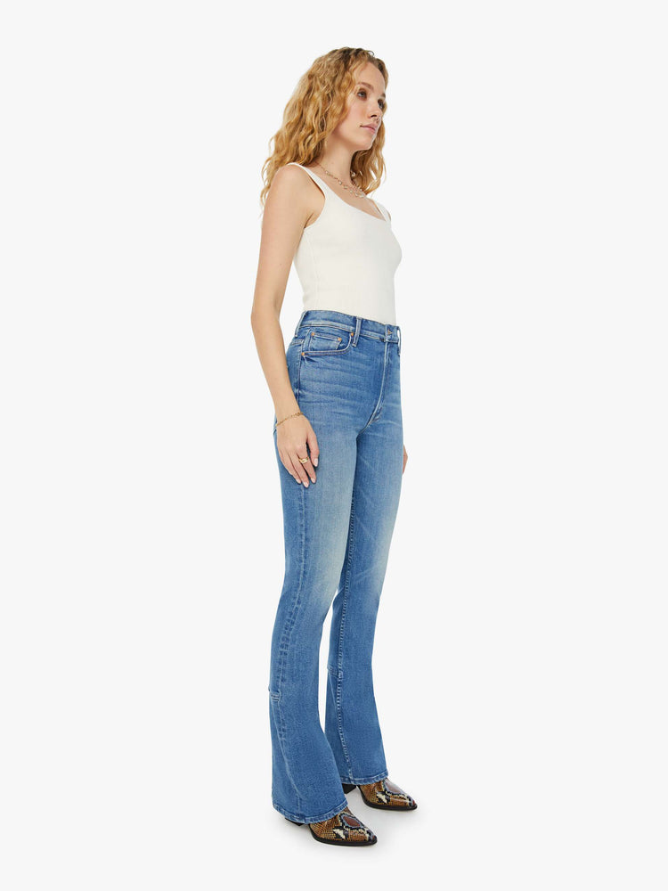 Angled view of a woman high-waisted skinny-flare jeans with a slightly dropped crotch, long 34-inch inseam, slits at the heels and a clean hem in a mid blue wash.