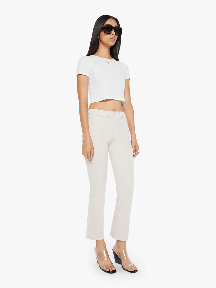 Side angle  view of a woman in a off white cream color mid-rise pants with a flared leg and a 28.25-inch inseam with a clean hem. 