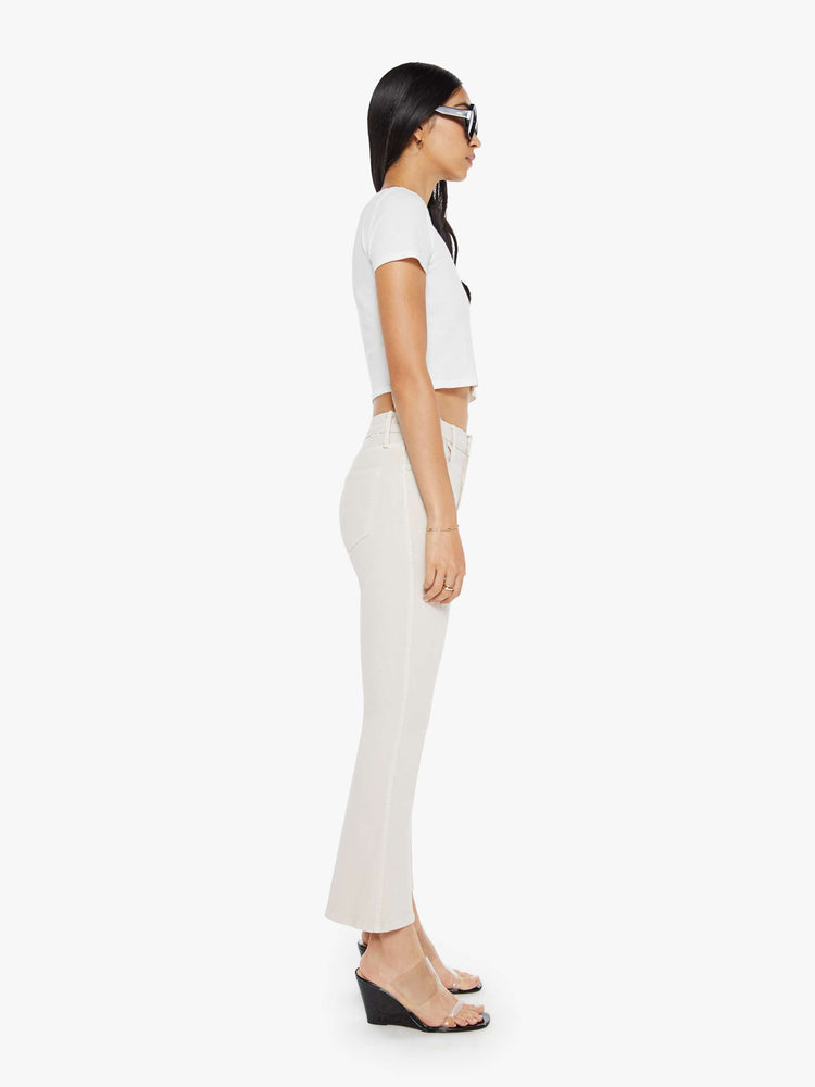 Side  view of a woman in a off white cream color mid-rise pants with a flared leg and a 28.25-inch inseam with a clean hem. 