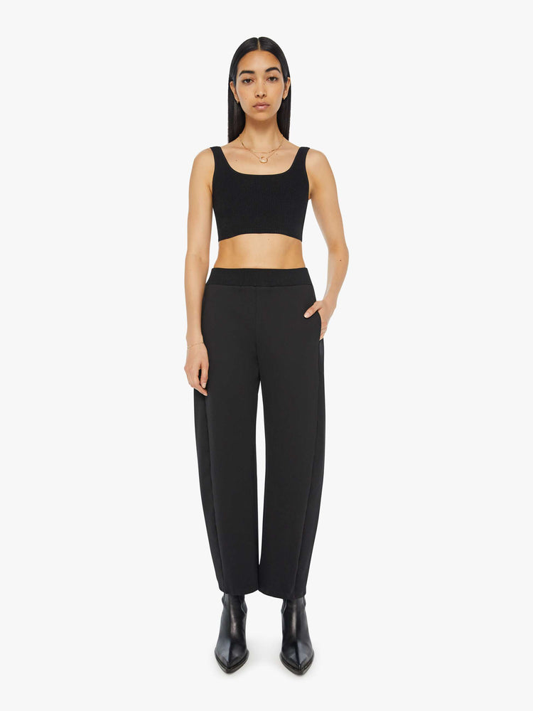 Front view of a woman in a black super high-waisted pants with a wide, curved leg, a thick elastic waistband, side slit pockets, a 28.25-inch inseam and a clean hem.