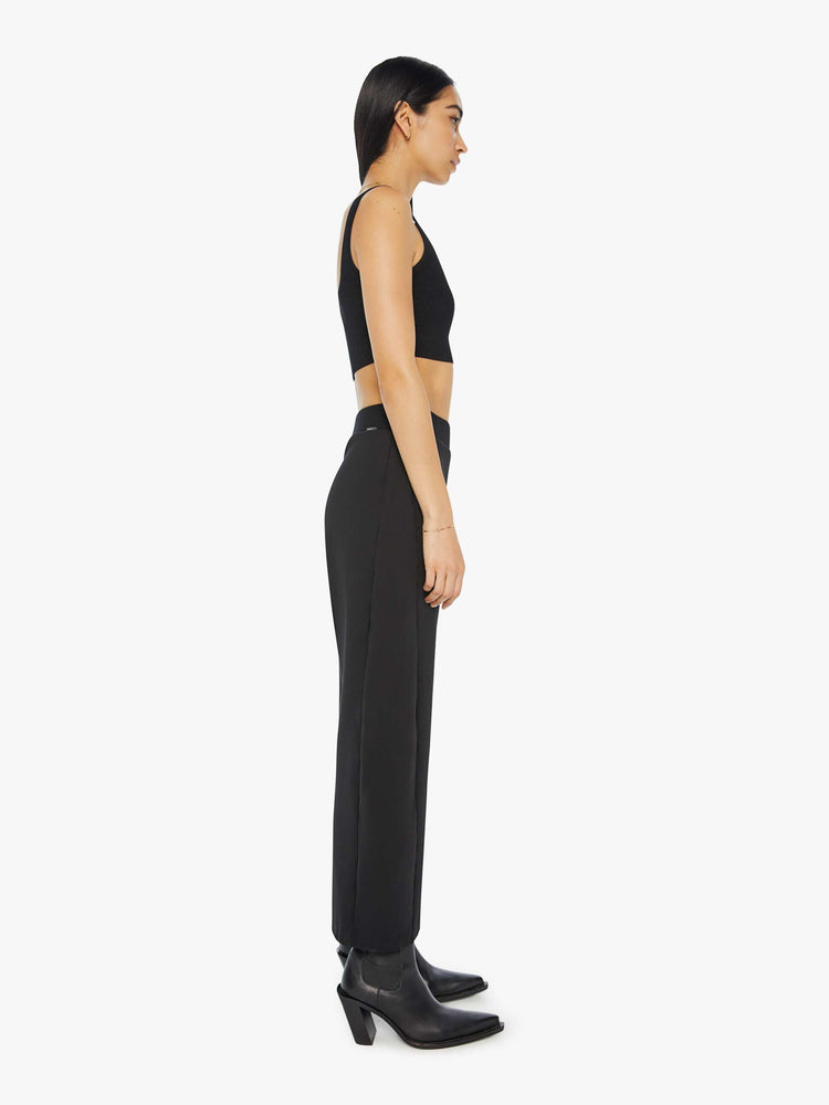 Side view of a woman in a black super high-waisted pants with a wide, curved leg, a thick elastic waistband, side slit pockets, a 28.25-inch inseam and a clean hem.