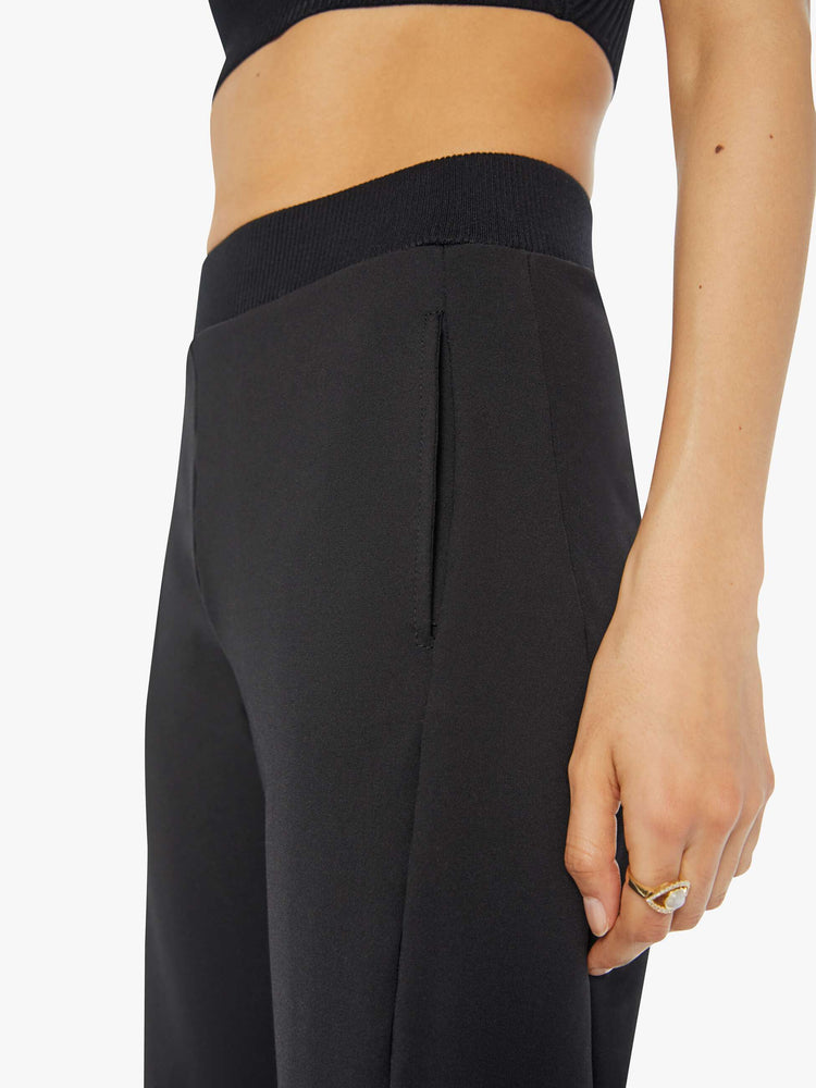 Waist view of a woman in a black super high-waisted pants with a wide, curved leg, a thick elastic waistband, side slit pockets, a 28.25-inch inseam and a clean hem.