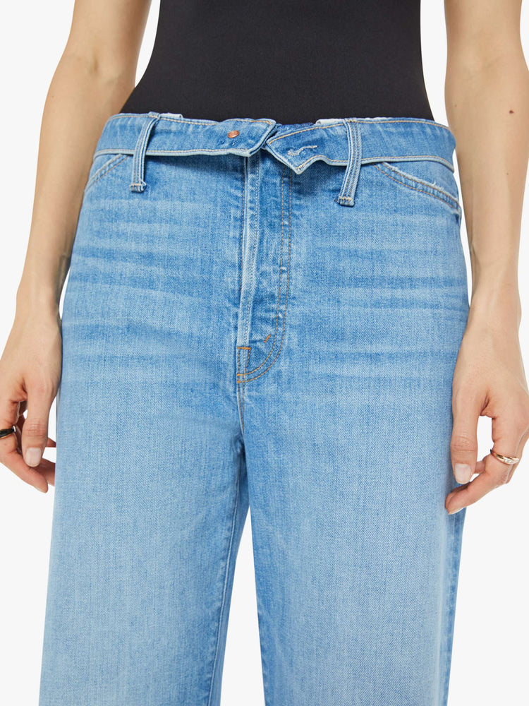 Waist view of a woman in mid blue wash high-rise, straight-leg jeans have a foldover waistband, long 32-inch inseam and a loose fit. 