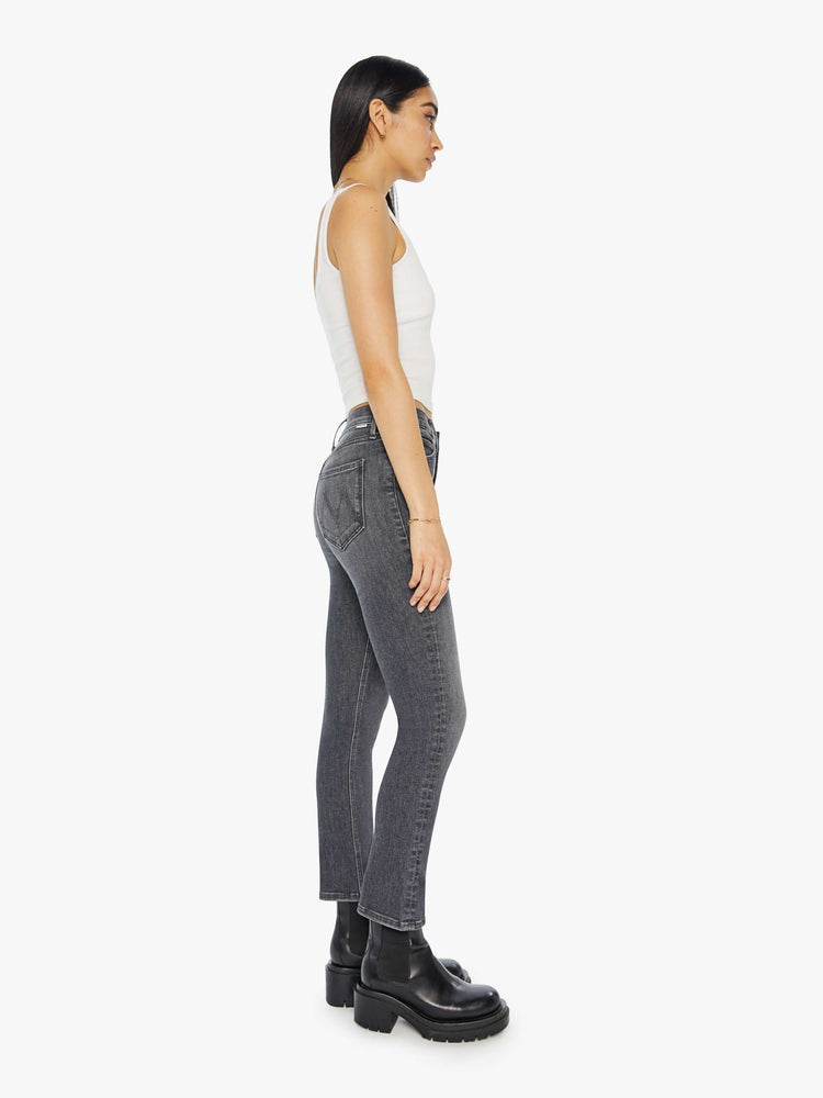 Side view of a woman in a dark grey mid rise straight leg jean with an exposed button fly and an ankle length inseam.