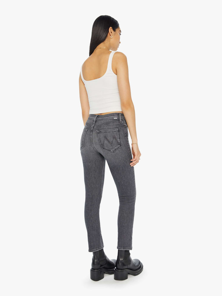 Back view of a woman in a dark grey mid rise straight leg jean with an exposed button fly and an ankle length inseam.