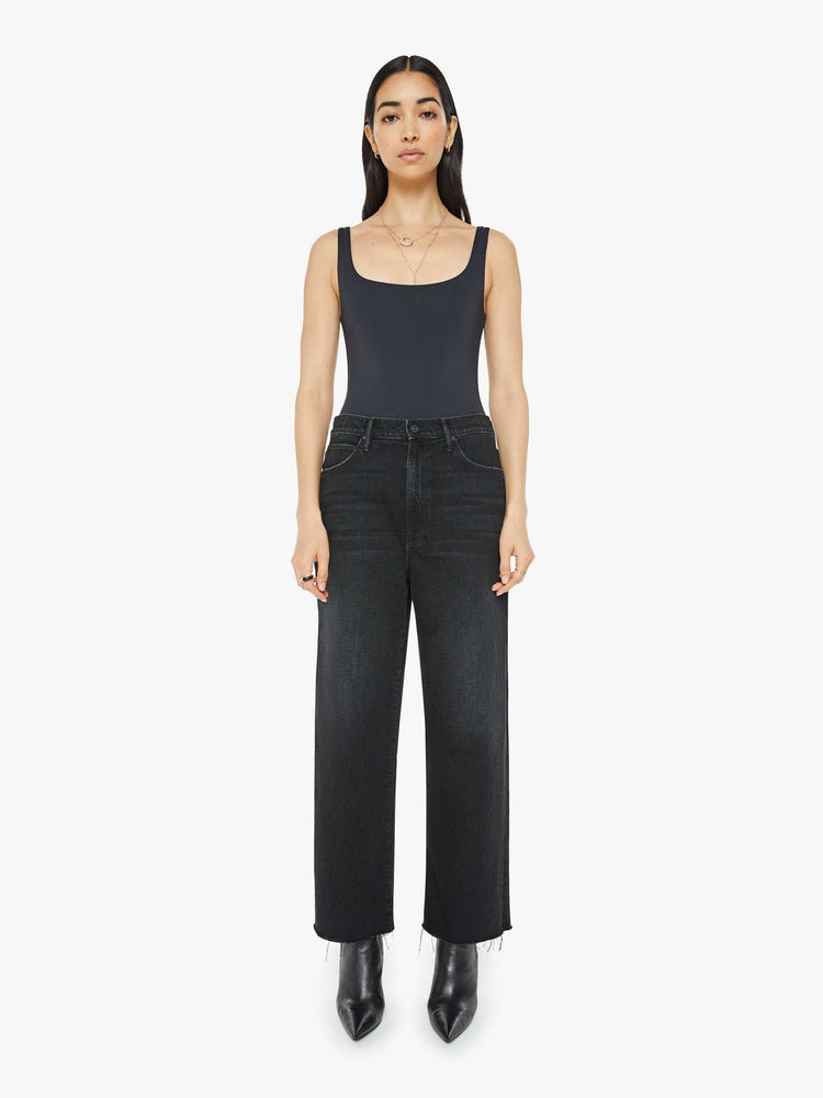 Front view of a woman in black  straight-leg jeans have an ankle-length inseam and a frayed hem. 