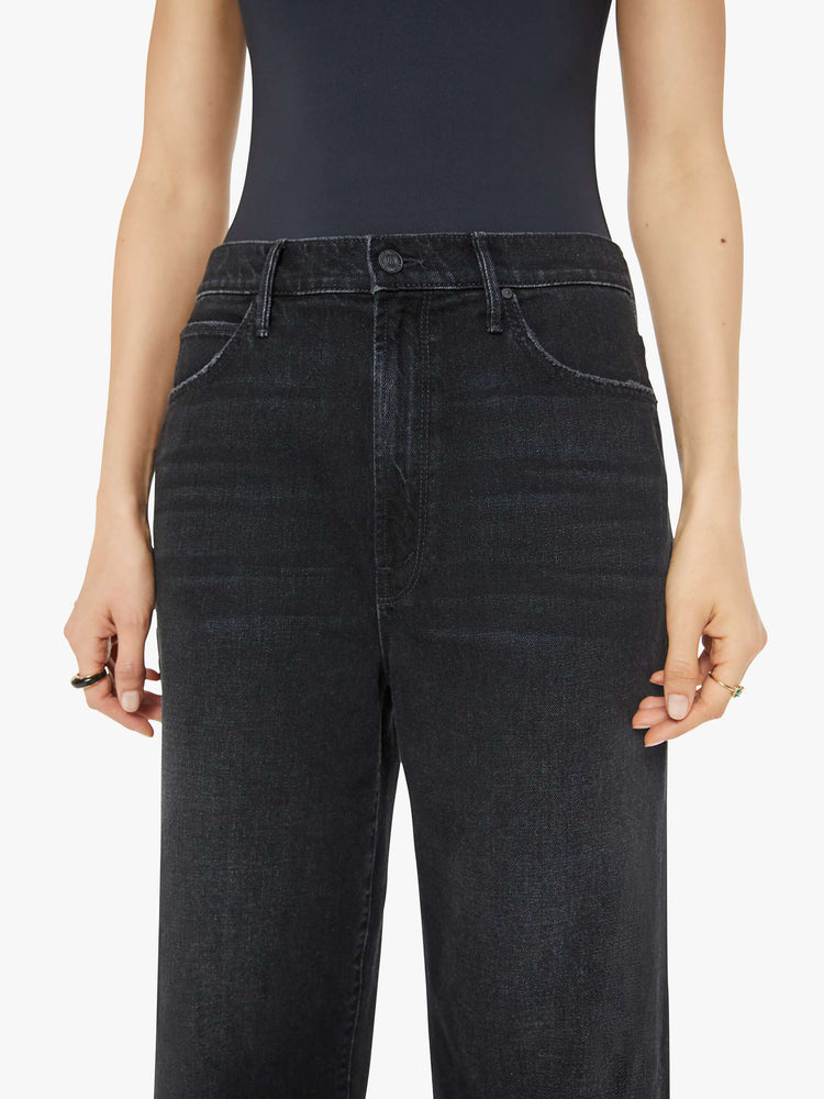 Waist close view of a woman in black  straight-leg jeans have an ankle-length inseam and a frayed hem. 