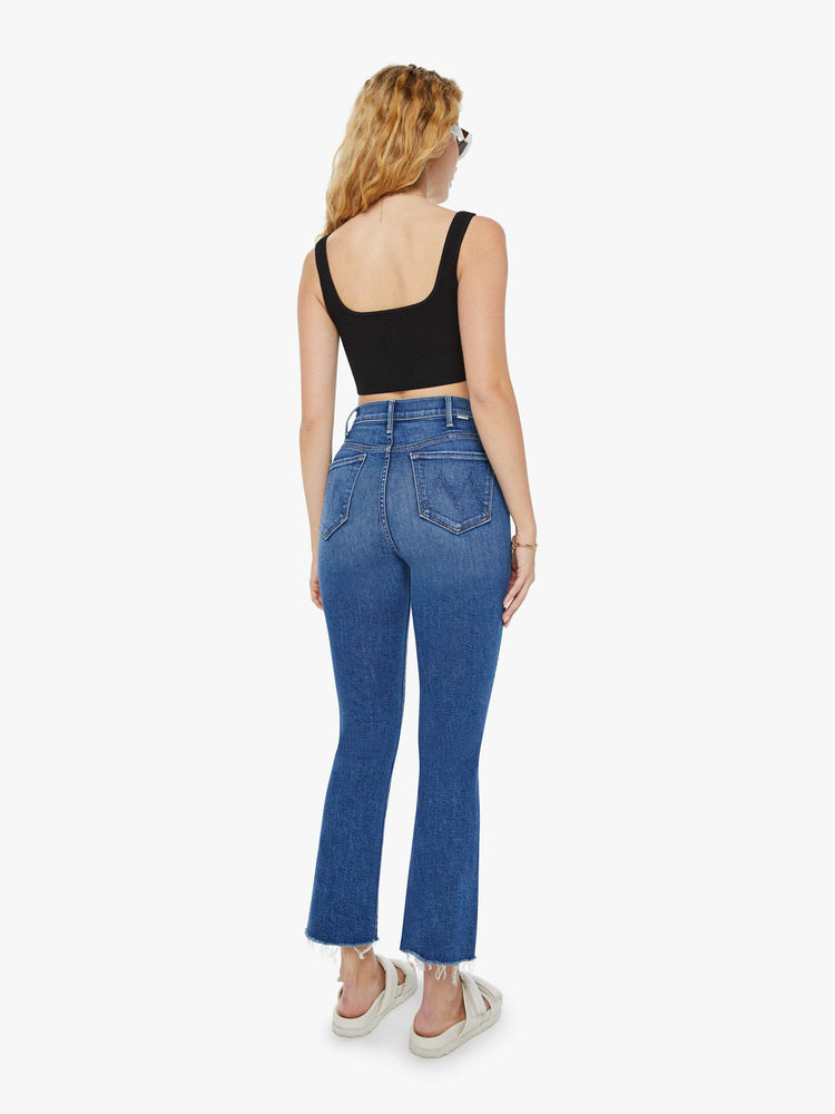 Back view of a woman in a med blue wash with a high-rise flare has an ankle-length inseam and a raw hem.