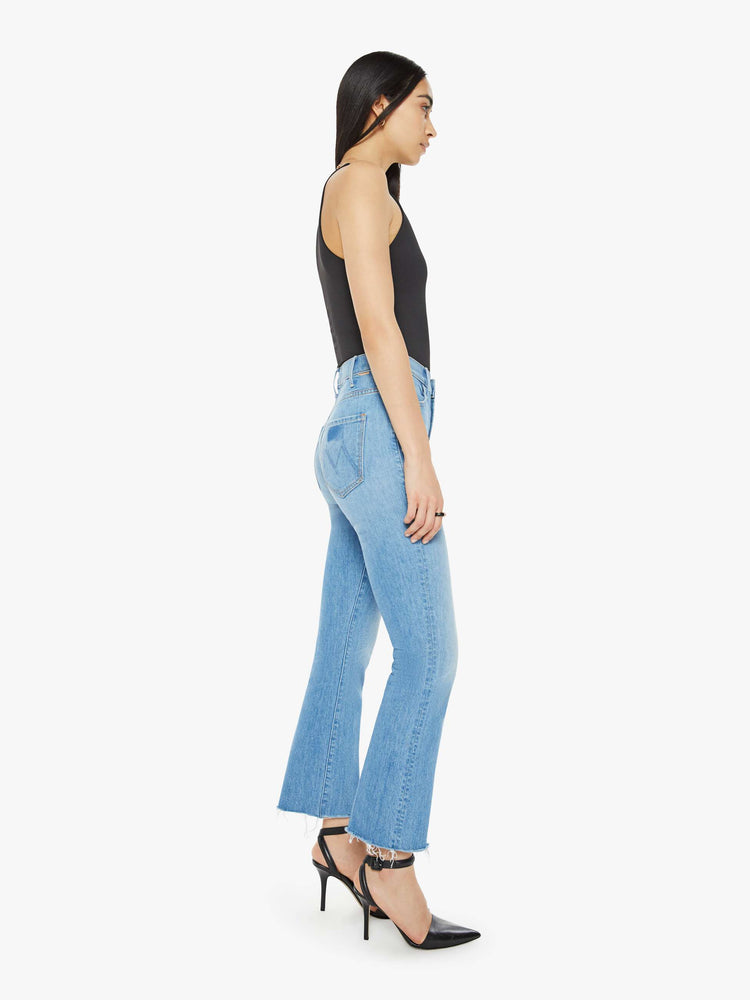 Side view of a woman in a mid blue wash high-rise bootcut has an ankle-length inseam and a raw hem.