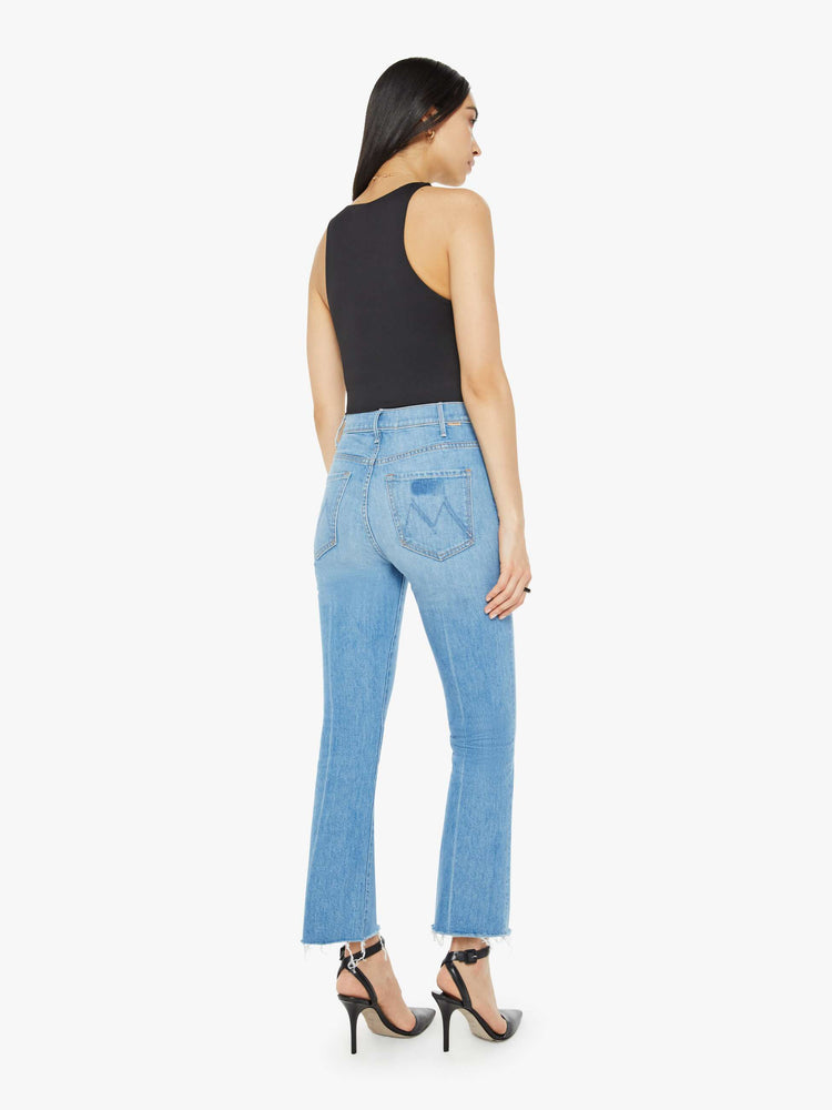 Back view of a woman in a mid blue wash high-rise bootcut has an ankle-length inseam and a raw hem.