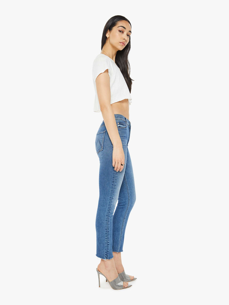 Side view of a woman mid blue  mid-rise straight leg with a 28.25-inch inseam and a frayed hem. 